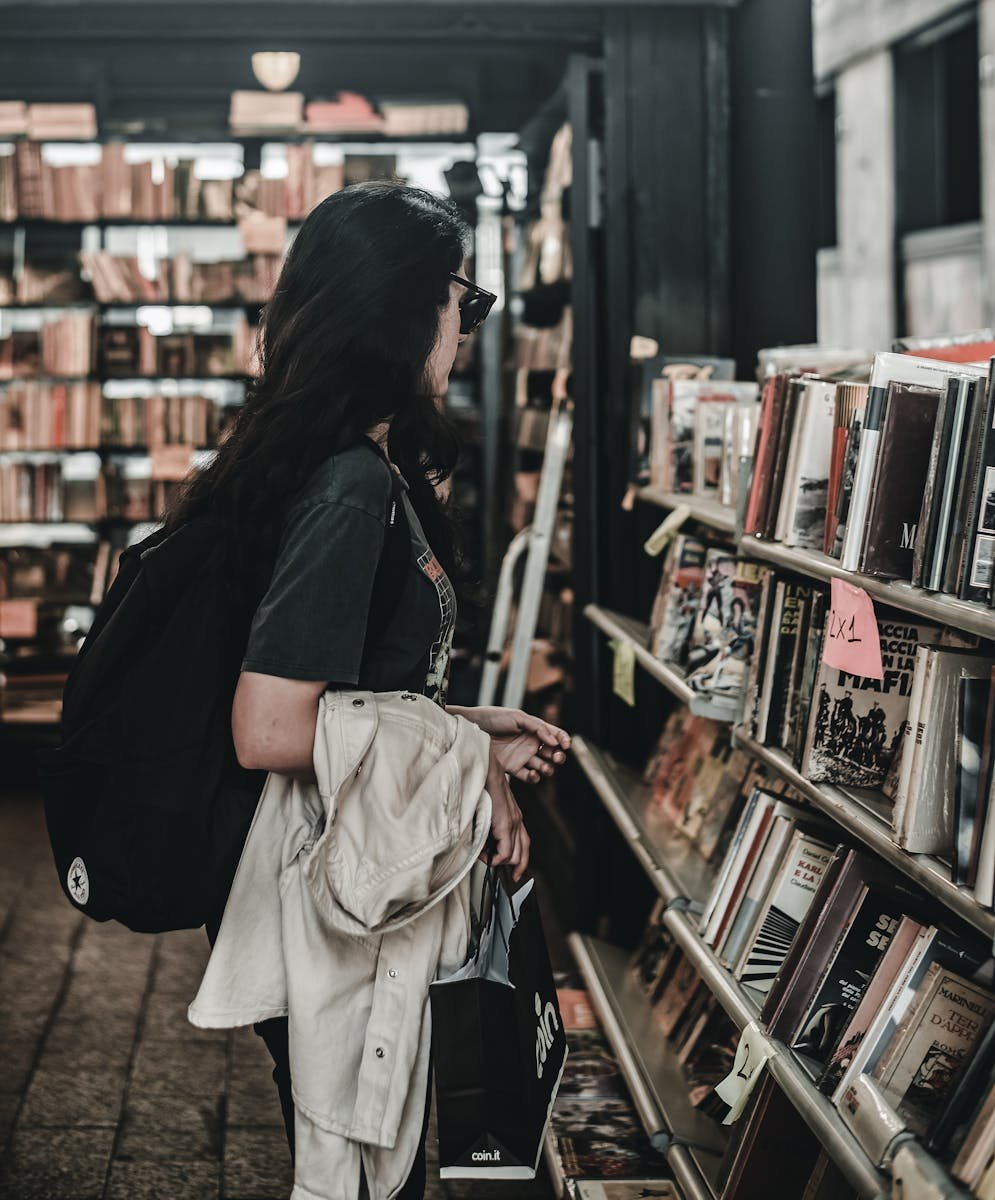 Woman in a bookstore in Genoa, Italy, exploring shelves of diverse literature. Cozy and intimate setting.